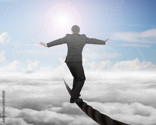 Businessman balancing on a wire with sky sub cloudscape