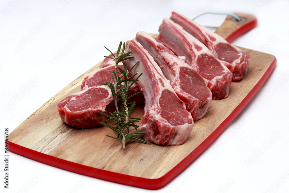Raw lamb cutlets with rosemary on chopping board white background Raw lamb cutlets with rosemary on chopping board white background
