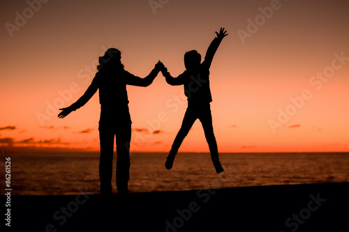 Silhouette of young mother having fun with her son, sunset