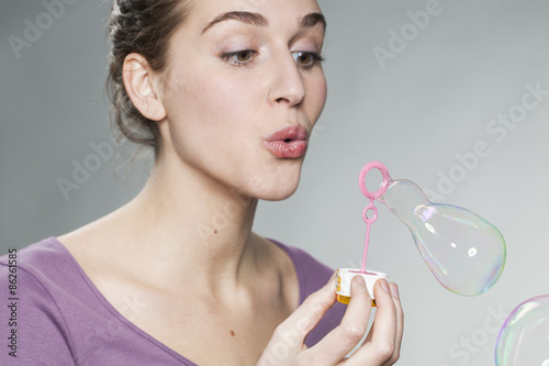 Canvas-taulu gorgeous young woman with purple sweater blowing bubbles on neutral background