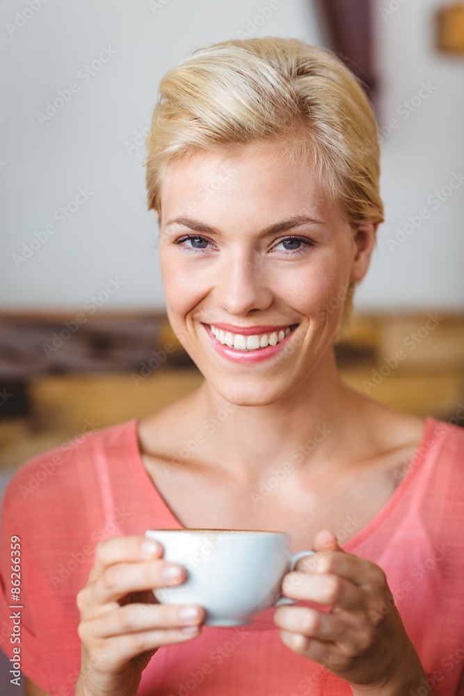 Pretty blonde woman smiling at camera and holding a cup of coffe Pretty blonde woman smiling at camera and holding a cup of coffe