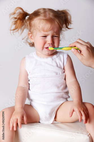 Crying baby getting her teeth cleaned with toothbrush