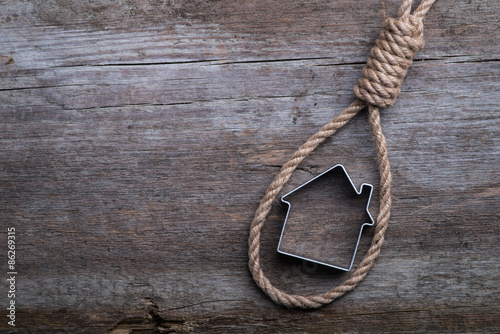 Small house framed with hangman's noose on brown wooden surface