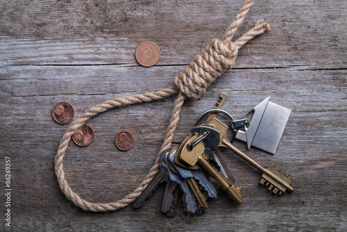 Hangman's noose with house, keys and money on brown wooden surface