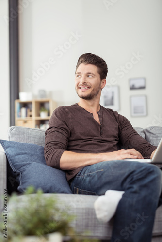 junger mann sitzt auf dem sofa mit seinem notebook