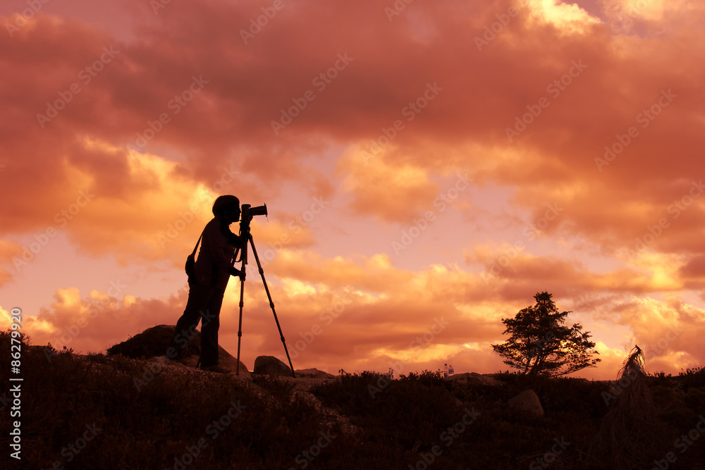 Silhouette of photographer taking photo in sunset on mountain top