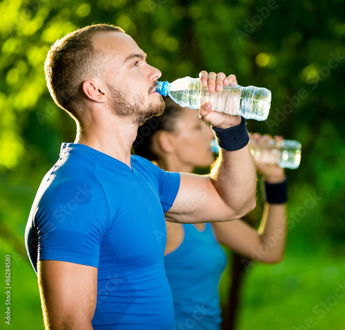 Man and woman drinking water from bottle after fitness sport