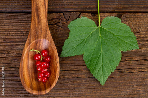 redcurrant in wooden spoon and leaf on wooden background