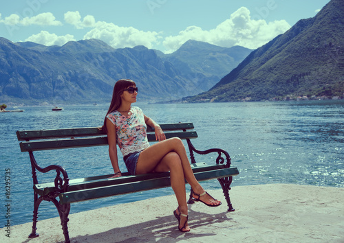 Beautiful young woman looking and waiting at the seacoast. Sunny day. Montenegro, Europe. Retro style toning image.