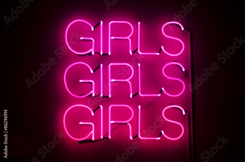 Girls Girls Girls sign glows in racy pink neon against dark night background