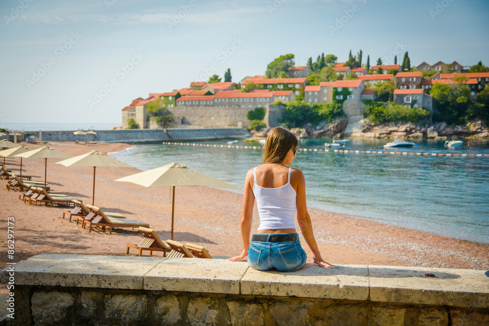 Beautiful young woman looking at the seascape and island Sveti Stefan. Montenegro, Europe.