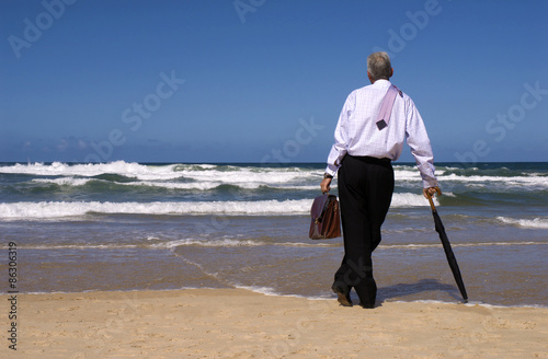 Business man or senior businessman dreaming of retirement on a sandy tropical beach umbrella and briefcase looking gazing in thought out to sea photo