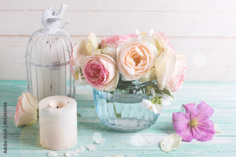 White roses, clematis and jasmine flowers in vase and candles in ray of light on turquoise wooden background against white wall. Place for text. Selective focus. White roses, clematis and jasmine flowers in vase and candles in ray of light on turquoise wooden background against white wall. Place for text. Selective focus.