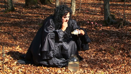 Dark Haired Woman In Black Tearing Dried Fish In Autumn Forest