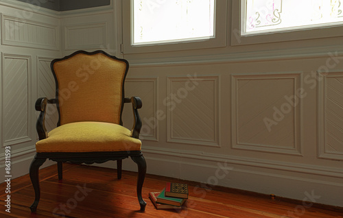 Fotografi Sillón torneado con libros al pie en penumbra junto a una ventana