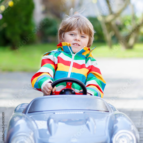 Little preschool boy driving big toy old vintage car, outdoors