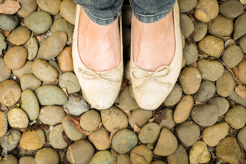 Fotografija Vintage closeup woman foot with cream shoes on stones background
