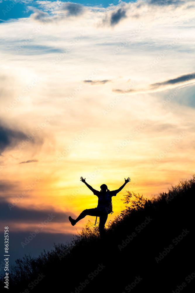 Happy female silhouette making funny dance.
Woman making dancing moves on steep grassy hill with gorgeous sunset sky and cloudscape on background