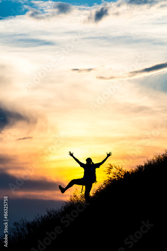 Happy female silhouette making funny dance.
Woman making dancing moves on steep grassy hill with gorgeous sunset sky and cloudscape on background