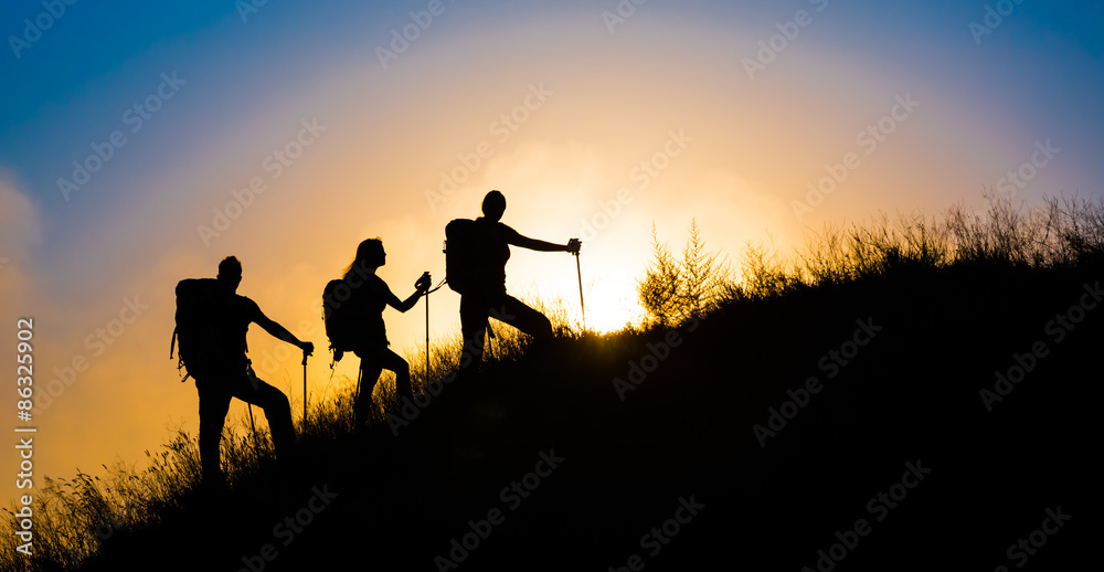 Climbers on grassy hill.
Family three people silhouette walking up steep grassy hill majestic sunrise and blue sky background