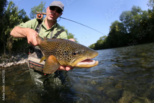 Closeup of fly-fisherman holding brown truit in river