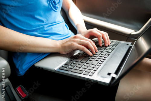 Unrecognizable businesswoman sitting in car with laptop computer on her knees. color image in horizontal orientation