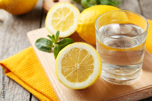 Lemons on cutting board with glass of water on grey wooden backg