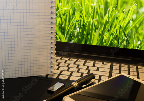 Office workplace with notebook, smart phone, pen, flash drive and wordpad with green grass background photo