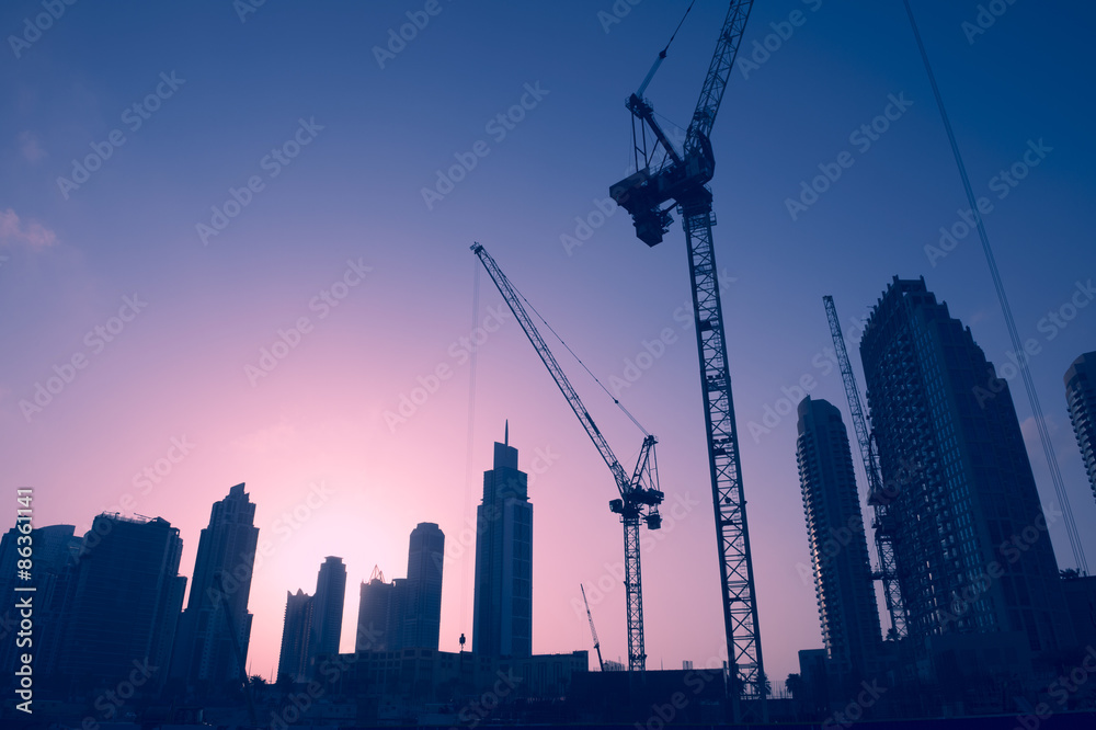 Obraz premium Panoramę słońca żurawi budowlanych wśród wieżowców biurowych w centrum handlu na Bliskim Wschodzie w Dubaju