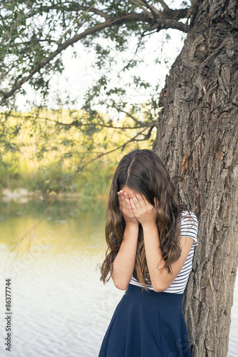 Teenage girl in the park covers his face