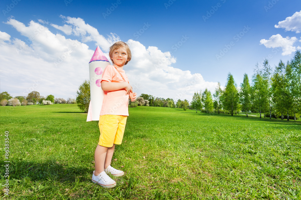 Standing boy wears paper rocket toy on shoulders Standing boy wears paper rocket toy on shoulders