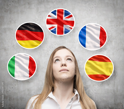 Beautiful lady is surrounded by bubbles with european countries' flags (Italian, German, Great Britain, French, Spanish). Learning of foreign languages concept. Concrete background. photo