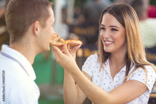 Beautiful young woman feeding her boyfriend with a slice of pizza