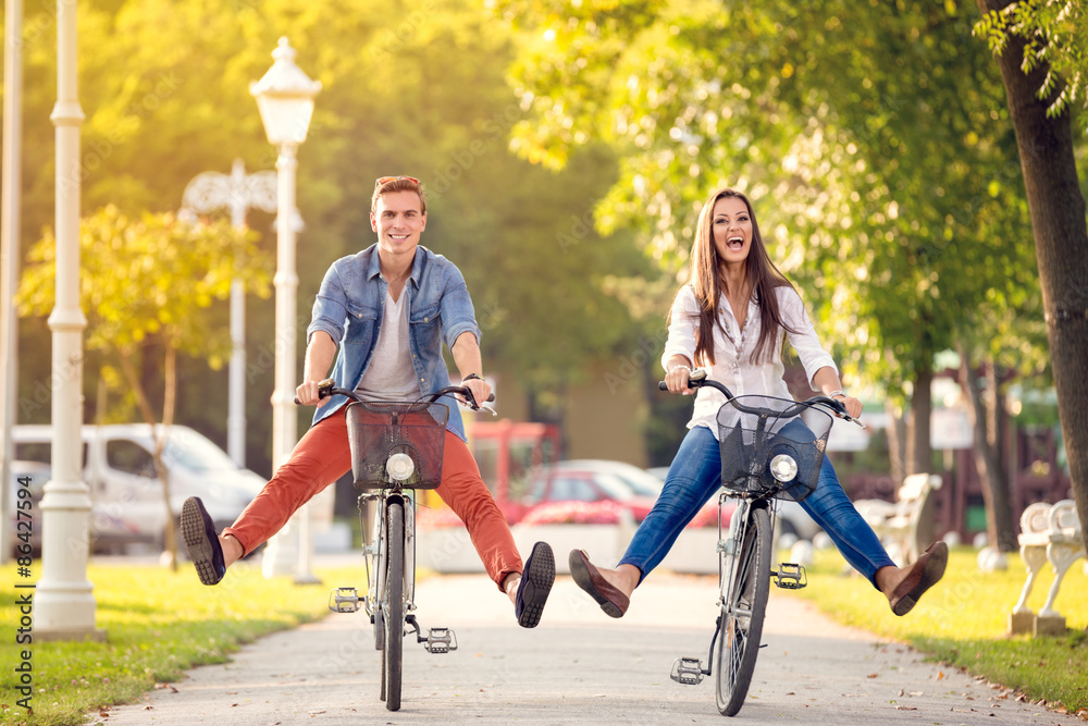 Happy funny couple riding on bicycle - obrazy, fototapety, plakaty 