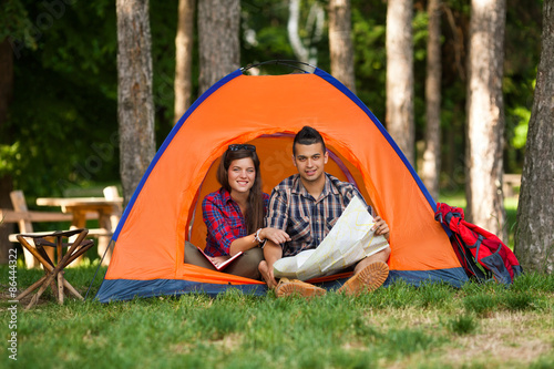 Smiling young couple sitting in a tent looking at maps and planning their camping trip