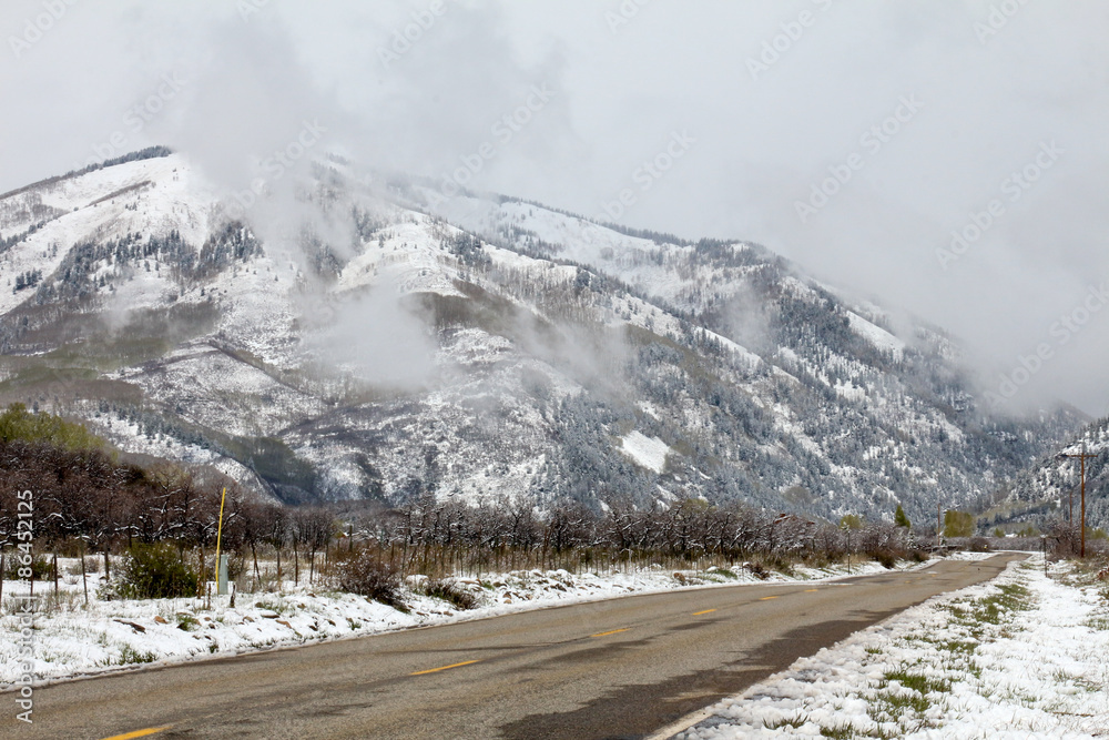 County road in Colorado that goes towards snow covered and cloud encased mountains