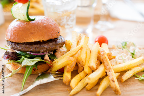 Hamburger with lettuce and french fries served on a wooden plate with a tight composition and short depth of field in a restaurant Environment.