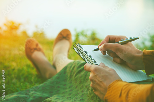 Fototapeta Naklejka Na Ścianę i Meble -  female hands with pen writing on notebook on grass outside