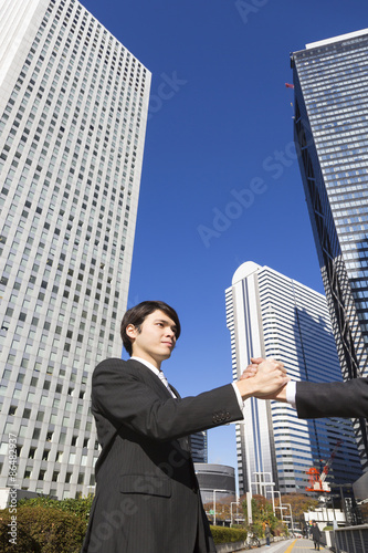 握手をするビジネスマン　　ローアングル　高層ビル背景