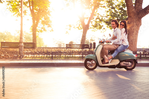 Cheerful young couple riding a scooter and having fun. Sun is shining in the morning