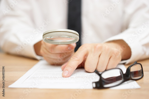 Focused businessman is reading through magnifying glass documen