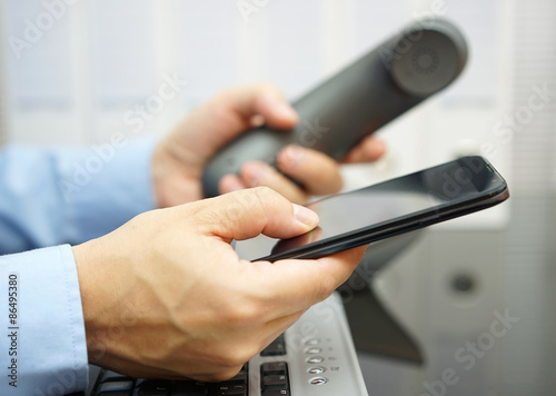 businessman is using smart mobile phone and land line telephone