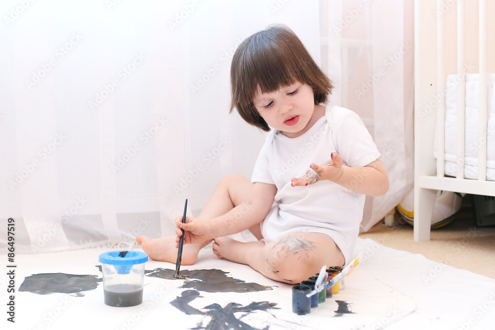 Cute child looks at dirty hands bedaubing with gouache Cute child looks at dirty hands bedaubing with gouache