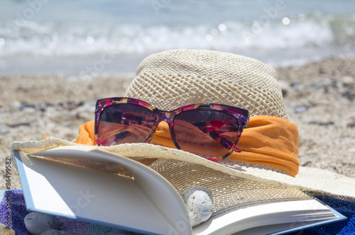Straw hat sunglasses and a book on the beach with sea in backgou photo