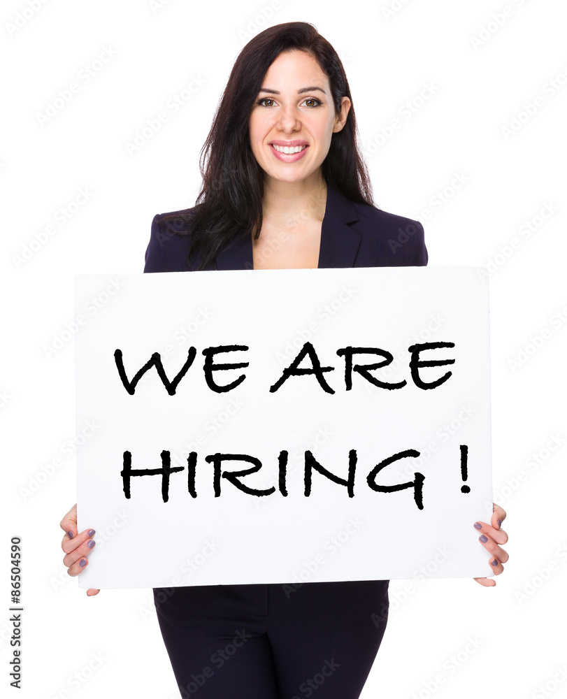 Young businesswoman holding a placard showing with we are hiring Young businesswoman holding a placard showing with we are hiring