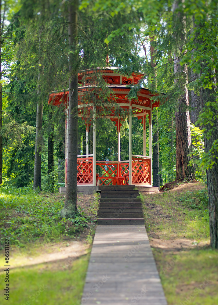 Red wooden gazebo in the forest.