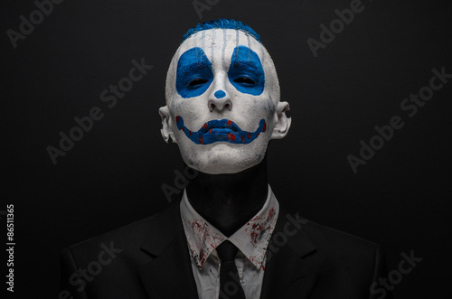 Terrible clown and Halloween theme: Crazy blue clown in black suit isolated on a dark background in the studio © Parad St