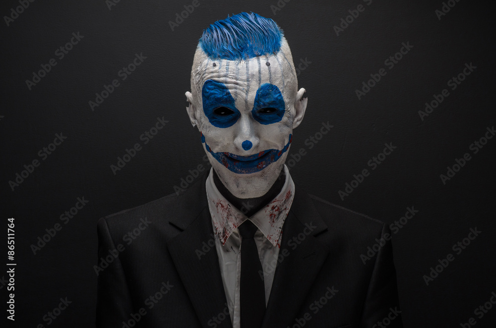 Terrible clown and Halloween theme: Crazy blue clown in black suit isolated on a dark background in the studio Terrible clown and Halloween theme: Crazy blue clown in black suit isolated on a dark background in the studio
