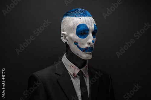 Terrible clown and Halloween theme: Crazy blue clown in black suit isolated on a dark background in the studio © Parad St