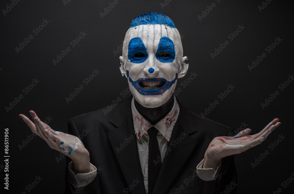 Terrible clown and Halloween theme: Crazy blue clown in black suit isolated on a dark background in the studio